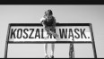 Wpadła bomba do piwnicy Grafika przedstawia czarno-biały kadr z teledysku, na którym widzimy małą dziewczynkę i tablicę Koszalińskiej Kolei Wąskotorowej