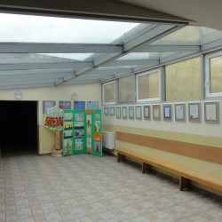 Szkoła Podstawowa nr 10 przed modernizacją energetyczną. Na zdjęciu widać korytarz. Po prawej stronie jest długa ławka. W rogu wystawiono prace dzieci, przeczepione do zielonej dużej kartki.