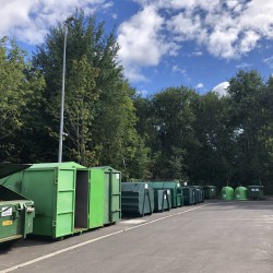 Kolorowy obrazek przedstawia od lewej szereg zielonych kontenerów na odpady zlokalizowanych w PSZOK przy ul. Na Skwierzynkę 2 w Koszalinie