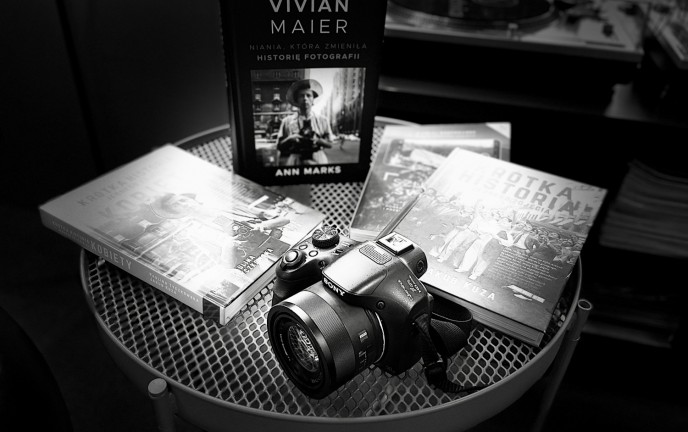 Czarno białe zdjęcie przedstawia aparat fotograficzny leżący na stoliku w towarzystwie książek.