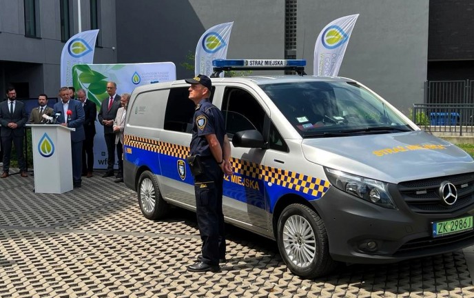 Prezydent Koszalina za mównicą. Na pierwszym planie nowe auto Straży Miejskiej wraz ze strażnikiem