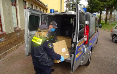 Dwoje Strażników Straży Miejskiej pakuje kartony z maseczkami ochronnymi do służbowego auta