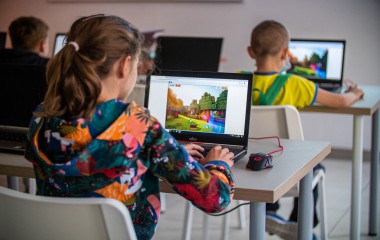 Dziewczynka w długich włosach siedząca na krześle i ucząca się programowania na laptopie