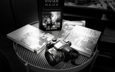 Czarno białe zdjęcie przedstawia aparat fotograficzny leżący na stoliku w towarzystwie książek.